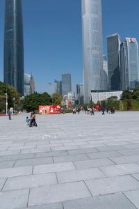 an outdoor plaza, filled with people walking around and tall buildings in the background,