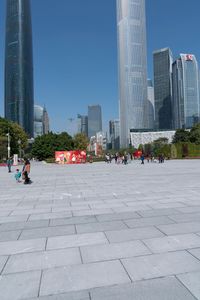 an outdoor plaza, filled with people walking around and tall buildings in the background,