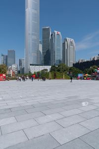 an outdoor plaza, filled with people walking around and tall buildings in the background,