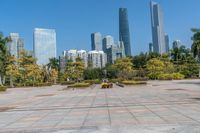 a park with a bench and large statue on the top of the concrete ground, with tall buildings in the back