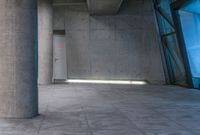 the interior of a building with glass and concrete walls and flooring, a grey door with red light on