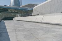 a man on a skateboard in an empty walkway near the cityscape of tall buildings