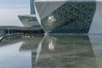 a large glass building is reflected in the water below it's glassy facade