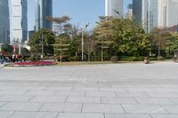 some people on an empty square surrounded by skyscrapers and green trees and shrubs in the foreground