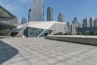 the building has glass and a steel structure in front of it, and several skyscrapers in the background