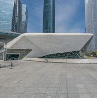 a person with a suitcase walks through a square in the city with a building that has a triangular shaped structure that appears to be a cube