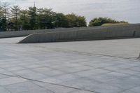 a person on a skateboard in an urban park next to concrete walls and trees