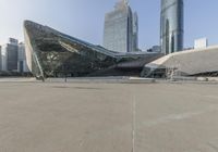 an open plaza with large buildings in the background and people on benches below it under a blue sky