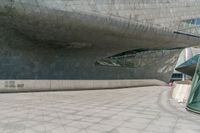 a man walks down the road in front of a large building with some glass walls