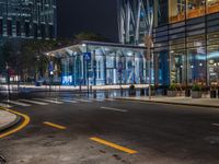 an empty city street with the lights turned on at night, and a large glass building in the background