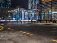 an empty city street with the lights turned on at night, and a large glass building in the background