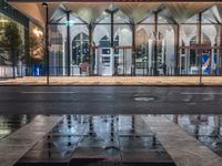 the reflection in the puddle is on the sidewalk next to a street with two large glass windows and three black blocks