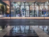 the reflection in the puddle is on the sidewalk next to a street with two large glass windows and three black blocks