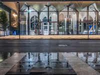 the reflection in the puddle is on the sidewalk next to a street with two large glass windows and three black blocks