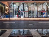 the reflection in the puddle is on the sidewalk next to a street with two large glass windows and three black blocks