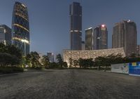 the skyscrapers are illuminated up on an empty road near buildings, including one of which is a public toilet