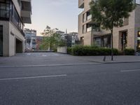 a man walks down the street near two buildings and trees and a parking lot at twilight