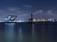 a body of water with a clock tower in the middle and lights on at the edge