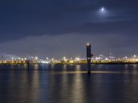 a body of water with a clock tower in the middle and lights on at the edge