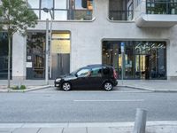 a small black car parked outside of a building on a street corner with cars in the middle