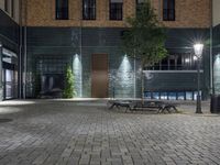 a empty bench is placed out in an empty courtyard with lights shining from behind the bench