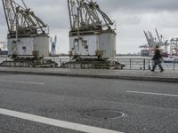 three large cranes standing in an open parking lot by the water near the waterfront and the sea