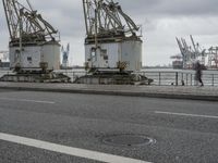 three large cranes standing in an open parking lot by the water near the waterfront and the sea
