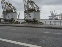 three large cranes standing in an open parking lot by the water near the waterfront and the sea