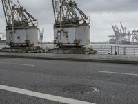 three large cranes standing in an open parking lot by the water near the waterfront and the sea