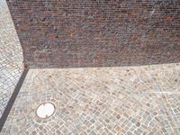 an empty street with a hole in the side and a brick wall with a pattern