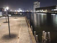 a brick walkway over a river next to buildings at night with lights on in the background