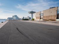 a skateboarder in the foreground, at the edge of a paved road with the city skyline in the background