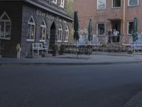 a woman on a bike driving down the street past an outdoor seating area and restaurant