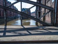 a metal gate with no one on it over an alley with buildings and water behind it