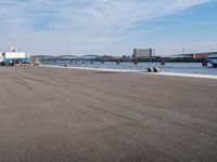 a long paved street in front of a bridge and water line with a boat docked on one side