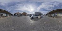 an empty road with parked cars and buildings on the side of it in front of a sky