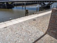 the view of the bridge from an area with brick walkways and water in background