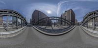 fisheye image taken on a bridge over street in front of tall buildings under blue skies