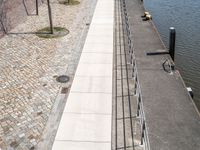 some people are walking along a path beside water and buildings with brick walls and plants in the foreground