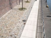 some people are walking along a path beside water and buildings with brick walls and plants in the foreground