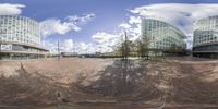 an unusual mirror in the middle of a square with multiple buildings behind it and some trees in the middle