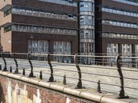 large brick building with tall glass and metal buildings behind it, near bridge over river