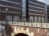 large brick building with tall glass and metal buildings behind it, near bridge over river