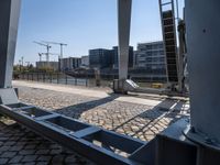 there is a steel guard rail in a large open area on the ground next to a river with buildings and construction crane