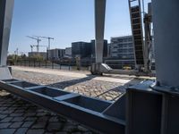 there is a steel guard rail in a large open area on the ground next to a river with buildings and construction crane