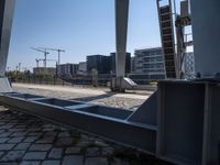 there is a steel guard rail in a large open area on the ground next to a river with buildings and construction crane