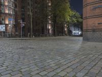 a brick sidewalk with cars parked along it at night in an old city street near tall buildings