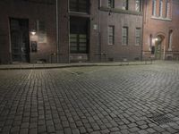 a black fire hydrant sitting on the side of a brick road near buildings with red lights