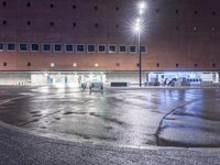 an empty parking lot next to a building at night time in the rain and illuminated by street lights