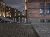 there is a bench sitting on the street with buildings in the background at night and street light